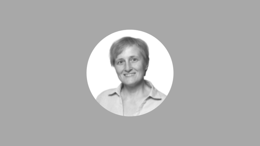 A grayscale headshot of a smiling person with short hair wearing a collared shirt, set against a solid gray background—perfect for attracting talent with its professional and approachable vibe.