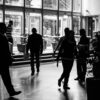 Silhouetted figures walk through a busy indoor lobby in a black and white composition.