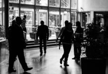 Job losses to hit manufacturing and retail as growth slows and energy costs rise Silhouetted figures walk through a busy indoor lobby in a black and white composition.