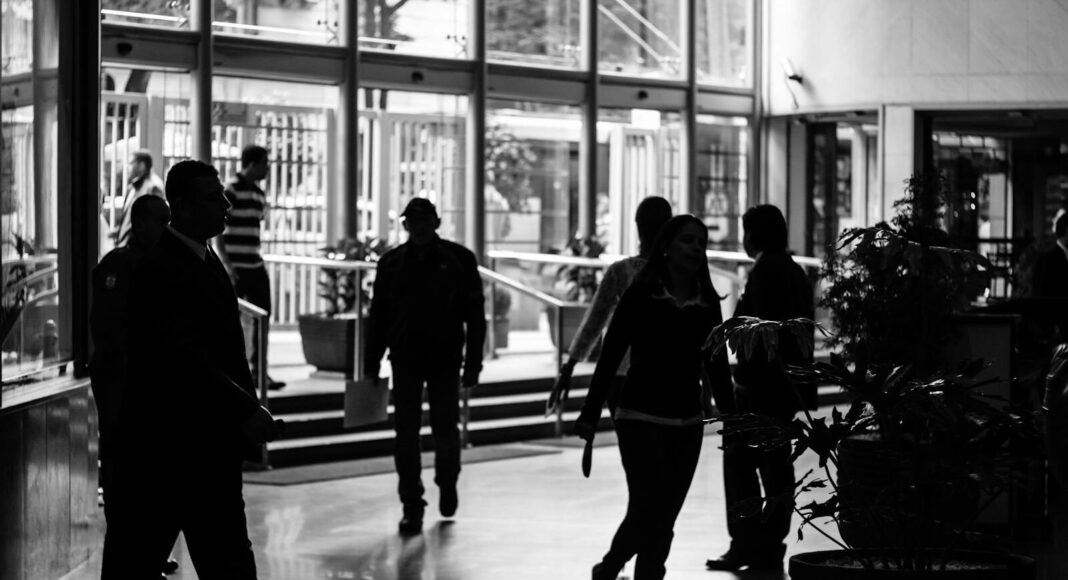 Silhouetted figures walk through a busy indoor lobby in a black and white composition.