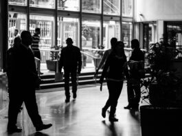 Unemployment rises to highest level in nearly five years as hiring slows Silhouetted figures walk through a busy indoor lobby in a black and white composition.