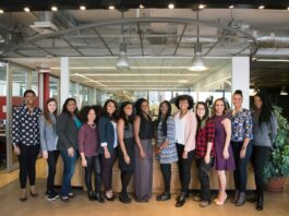 A diverse group of women in technology poses together in an office lobby, exuding confidence and teamwork.