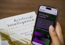 Employers urged to rethink race for chief AI officers Close-up of a smartphone displaying ChatGPT app held over AI textbook.