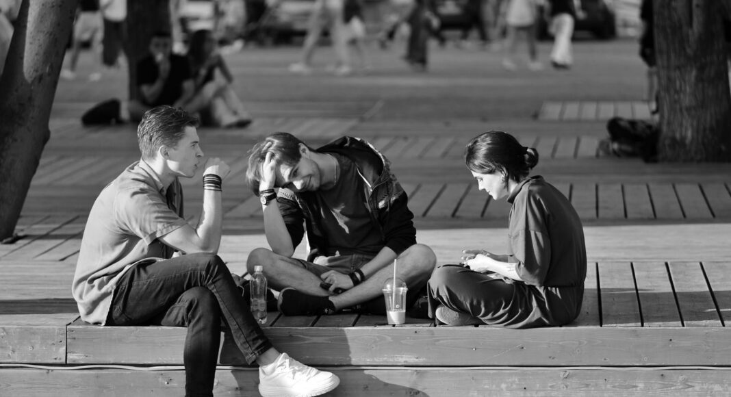 Three young adults sitting on a bench in a vibrant urban setting.