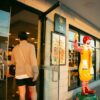 A man in casual attire enters a McDonald's restaurant, past a Ronald McDonald statue, during daylight.