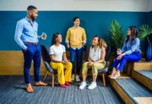 Warning over lack of manager training to support neurodivergent staff A diverse group of five professionals engaging in a casual indoor meeting, smiling and talking.