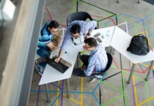 Employers warn against ban on non-compete clauses in jobs Three men collaborating over a laptop in a modern, geometric-themed office space.