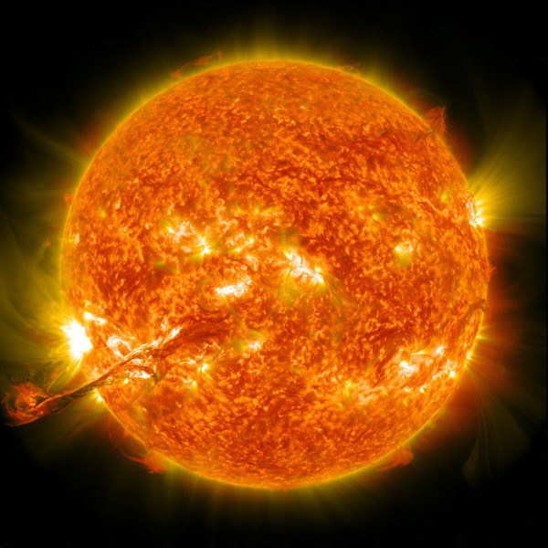 An image of the Sun with visible solar flares and prominences emanating from its surface, resembling a cosmic heatwave against a black space background.