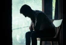 Mental health ‘stigma’ still stops staff speaking to managers A man sits alone in a moody indoor setting, silhouetted against a bright window, deep in thought.