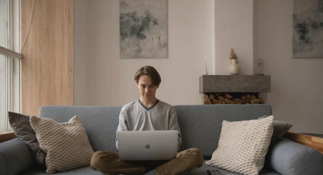Man sitting on a couch using a laptop in a home setting.