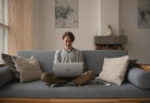 Nearly half of workers plan to quit as remote staff refuse return to office ‘at any salary’ Man sitting on a couch using a laptop in a home setting.