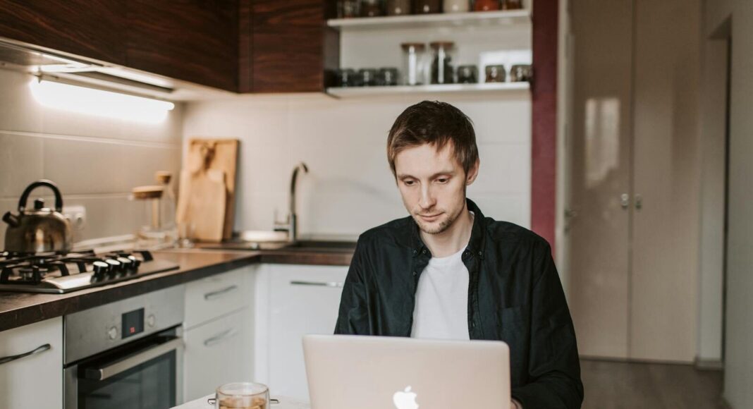 A man works on a laptop at a kitchen table.