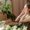 A woman relaxes, massaging her temples among indoor plants in a bright, sunlit room.