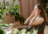 ‘Nearly half of employers lack formal wellbeing strategy’, raising concerns over support A woman relaxes, massaging her temples among indoor plants in a bright, sunlit room.