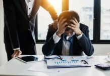 Millions of workers affected by ‘secondhand stress’ from colleagues An overwhelmed businessman grasps his head, surrounded by reports in a bright office.