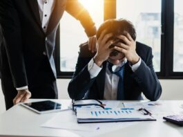 Millions of workers affected by ‘secondhand stress’ from colleagues An overwhelmed businessman grasps his head, surrounded by reports in a bright office.