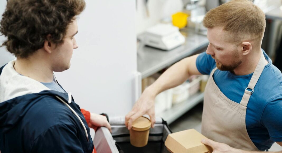 A delivery worker getting a food order from a man in a restaurant.