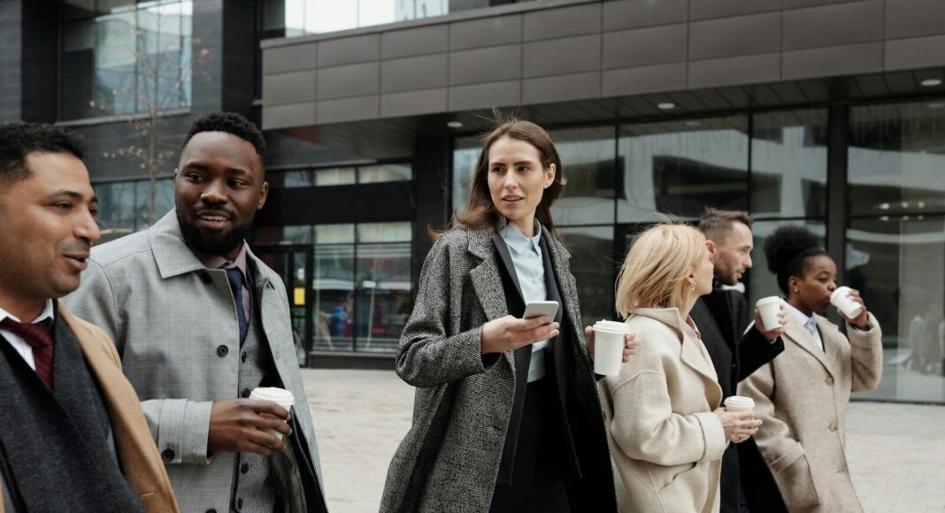 Photo by August de Richelieu A diverse group of business professionals walking outside a modern building, enjoying coffee and conversation.