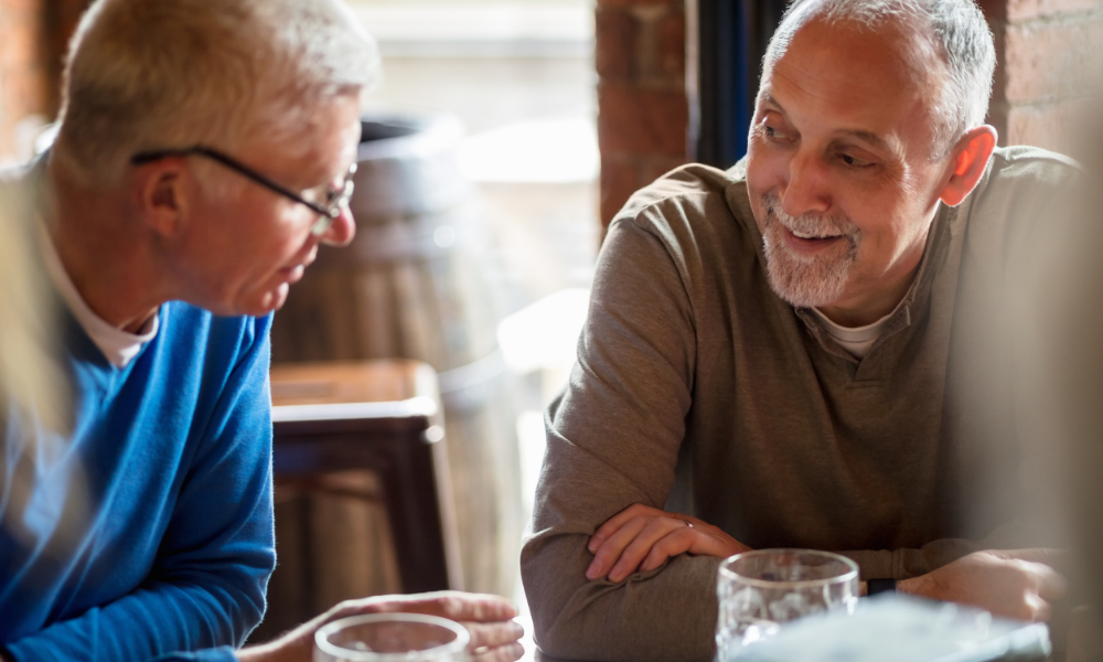 two men over 50 chatting at a cafe with drinks in front of them