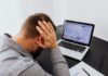 Fear of becoming obsolete grips workers as AI reshapes careers A man with his hands on his head, indicating stress and worries, sits in front of a desk with a laptop.