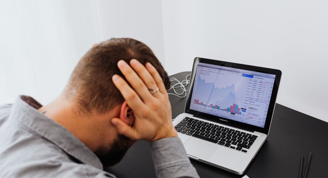 Photo by www.kaboompics.com A man with his hands on his head, indicating stress and worries, sits in front of a desk with a laptop.