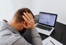 Fear of becoming obsolete grips workers as AI reshapes careers A man with his hands on his head, indicating stress and worries, sits in front of a desk with a laptop.