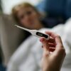 Hand holding a digital thermometer with blurred background of a sick person.