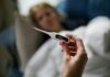 Firms warn sick pay changes could drive costs up as many remain unprepared Hand holding a digital thermometer with blurred background of a sick person.