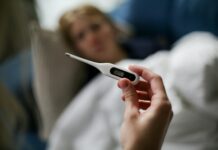 Firms warn sick pay changes could drive costs as many remain unprepared Hand holding a digital thermometer with blurred background of a sick person.