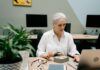 Women ‘uncomfortable’ discussing menopause at work as brain fog affects performance An older woman multitasking with lunch and work on laptop in an office setting.