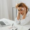 A woman in distress at her office desk, surrounded by tissues and a laptop.