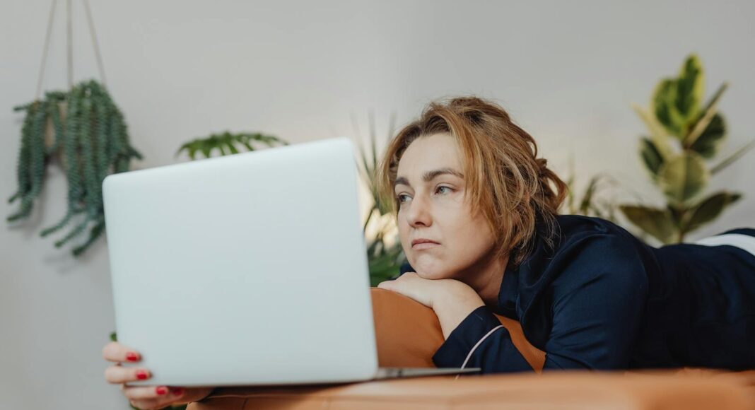 Photo by Karolina Grabowska www.kaboompics.com A woman lying on a couch indoors, looking upset while holding a laptop in a cozy home environment.