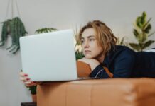 Millions unhappy at work as two-thirds consider retraining, study suggests A woman lying on a couch indoors, looking upset while holding a laptop in a cozy home environment.