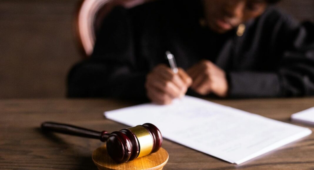 Judge signing documents at desk with focus on gavel, representing law and justice.