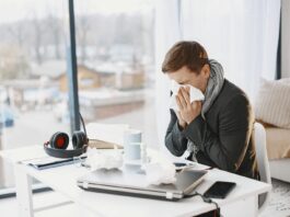 Sick pay overhaul set to reshape workplaces as reforms take hold Man sneezing at home desk, indicating remote work during illness.