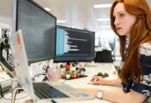 Government launches tech jobs drive to bring more women into the sector A young woman works at a desk with two monitors and a laptop.