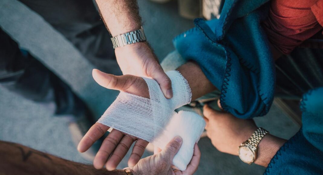 Close-up of two people bandaging an injured hand outdoors, focusing on first aid care.