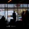 Silhouettes of travelers waiting at an airport terminal with an airplane visible through the window.