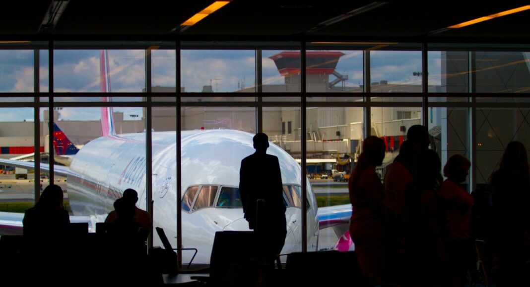 Silhouettes of travelers waiting at an airport terminal with an airplane visible through the window.