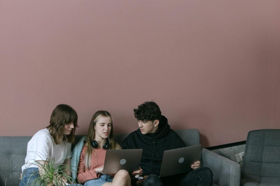 Three young adults collaborating with laptops in a cozy indoor setting.