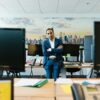 A businessman in a suit stands confidently in a modern office setting with crossed arms.