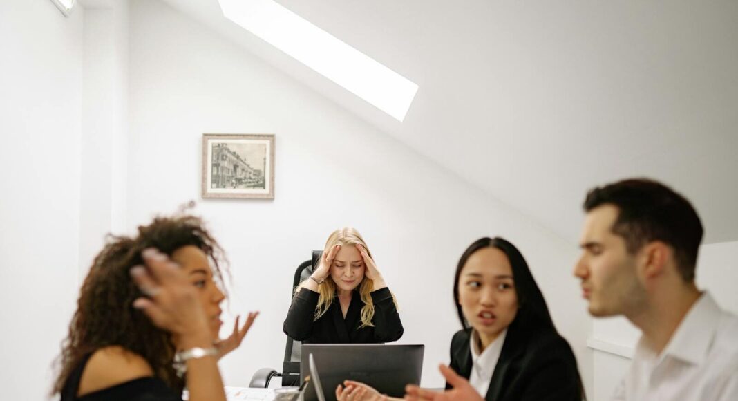 Colleagues in a heated discussion around a desk, highlighting workplace stress and tension.