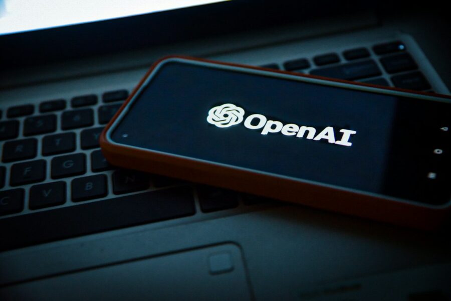 A phone displaying the OpenAI logo on top of a laptop.