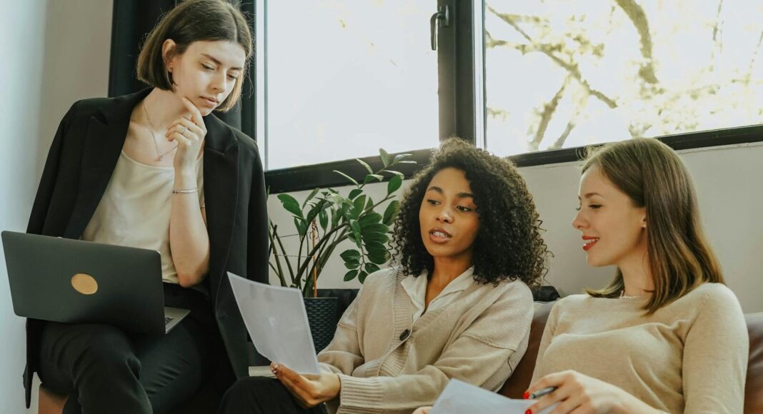 Three professional women engaged in a collaborative meeting in a modern office setting.