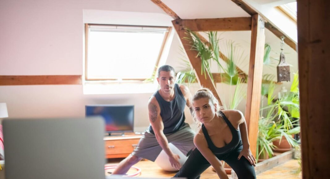 A man and woman working out at home using a laptop for guided exercises. Indoor active lifestyle.