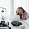 Frustrated woman sitting at desk with laptop, showing stress in a modern office environment.