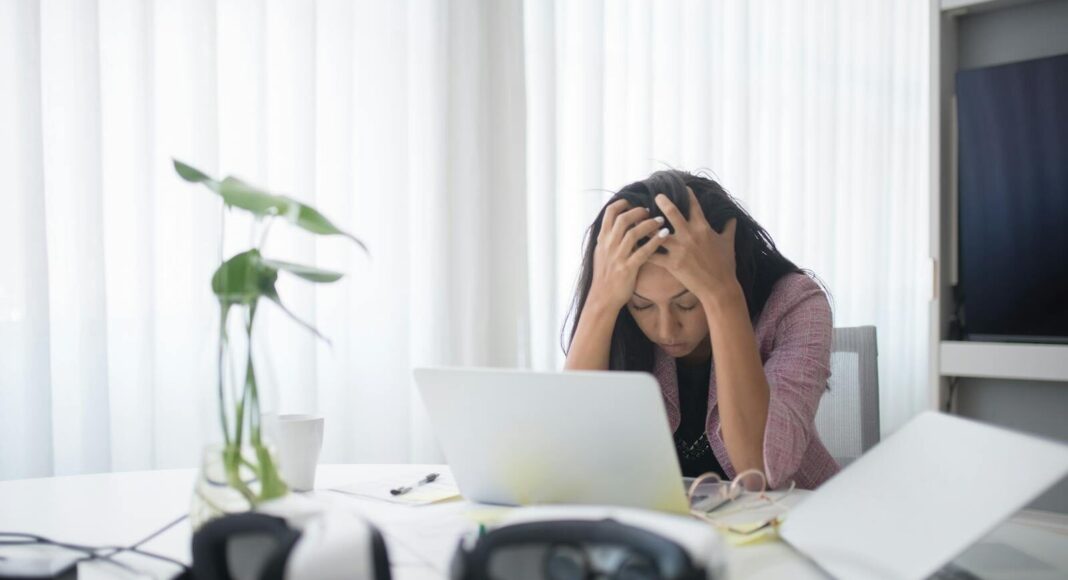Frustrated woman sitting at desk with laptop, showing stress in a modern office environment.