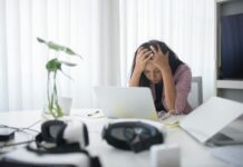 Mental health cited in a third of sickness absence cases ahead of sick pay changes Frustrated woman sitting at desk with laptop, showing stress in a modern office environment.