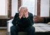 Workers say staying in the wrong job is their biggest career mistake An elderly man sitting on a bed indoors, expressing regret with his head in his hands.