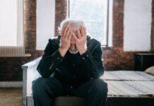 Workers say staying in the wrong job is their biggest career mistake An elderly man sitting on a bed indoors, expressing regret with his head in his hands.